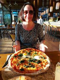 Inka Gluschke sitzt in einem Lokal, eine riesige Pizza steht vor ihr auf dem Tisch.