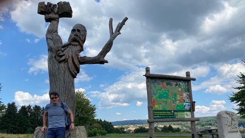 Uwe Becker vor einer aus einem Baumstamm geschnitzten Riesenfigur.