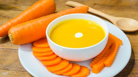 Karottensuppe ist mit rohen Möhren auf einem Teller arrangiert