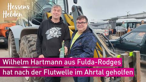 Wilhelm Hartmann und Olaf Trägler vor Baumaschinen. Wilhelm Hartmann mit einer Weinflasche von der Ahr (We AHR family).