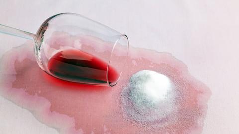 Ein umgekipptes Glas Rotwein hat einen Fleck gemacht, auf den Salz gestreut wurde.